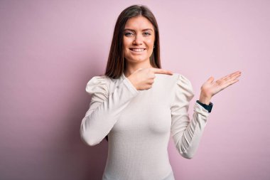 Mavi gözlü genç bir kadın pembe arka planda sıradan beyaz tişörtler giyiyor kameraya hayret ediyor ve gülümsüyor..