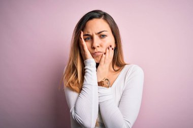 Pembe arka planda beyaz tişört giyen, mavi gözlü genç, güzel sarışın kadın. Yüzü, depresyonu ve üzüntüyü örten eller, sorun için üzgün ve tedirgin.