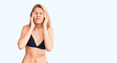 Elleri kafasında bikini giyen genç, güzel sarışın kadın, stres yüzünden baş ağrısı çekiyor. migren ağrısı. 