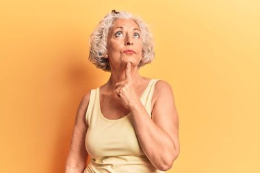 Kıdemli, gri saçlı, günlük kıyafetler giyen, şüpheyi düşünen, çenesinde parmak olan ve kafasını kaldırıp merak eden bir kadın. 