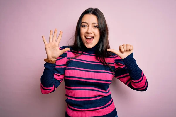 年轻的黑发优雅女人 穿着条纹衬衫 穿着粉色孤立的背景 带着自信和快乐的笑容 用手指指了指六号 — 图库照片
