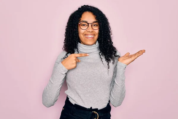 Młoda Afroamerykanka Swetrze Okularach Różowym Tle Zdumiona Uśmiechnięta Aparatu Wskazując — Zdjęcie stockowe