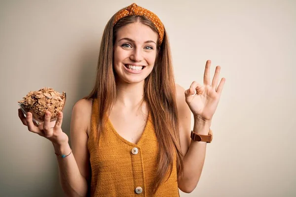若い美しい赤毛の女性は 指でOkサインを行う健康なコーンフレークシリアルのボウルを保持します 優れたシンボル — ストック写真