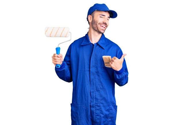 Jovem Hispânico Homem Vestindo Pintor Uniforme Segurando Rolo Apontando Polegar — Fotografia de Stock