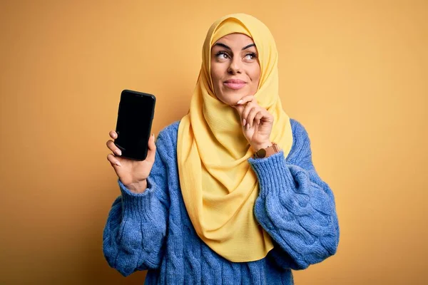 年轻美丽的黑发阿拉伯女人 头戴伊斯兰头巾 手持智能手机 脸上露出严肃的表情 思考着问题 非常混乱的想法 — 图库照片