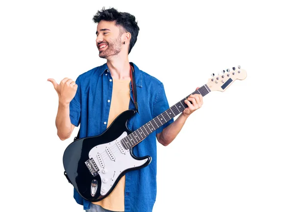 Joven Hispano Tocando Guitarra Eléctrica Apuntando Con Pulgar Hacia Costado — Foto de Stock