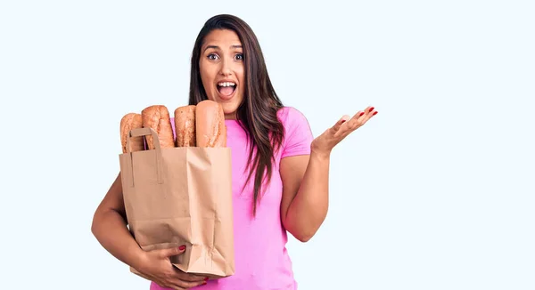Young Beautiful Brunette Woman Holding Delivery Bag Bread Celebrating Victory — Stock Photo, Image