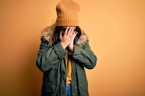 泣きながら手で顔をカバー悲しい表情で黄色の孤立した背景に帽子とメガネと冬のコートを身に着けている若いブルネットの女性 うつ病の概念 — ストック写真