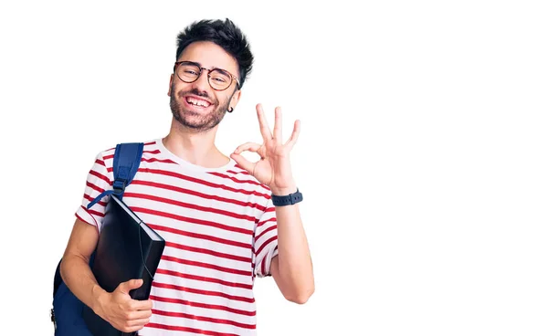 若いヒスパニック系の男は 学生のバックパックと眼鏡を保持バインダーを身に着けています指でOkサインを行います 笑顔優しいジェスチャー優れたシンボル — ストック写真