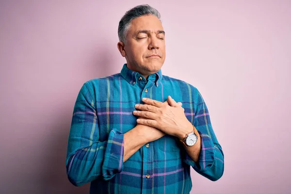 Middle age handsome grey-haired man wearing casual shirt over isolated pink background smiling with hands on chest with closed eyes and grateful gesture on face. Health concept.