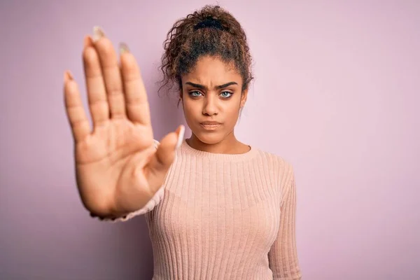 ピンクの背景の上に立つカジュアルなセーターを着た若い美しいアフリカ系アメリカ人の女の子は 手の手のひらで歌うのをやめます 顔に負と深刻なジェスチャーで警告式 — ストック写真