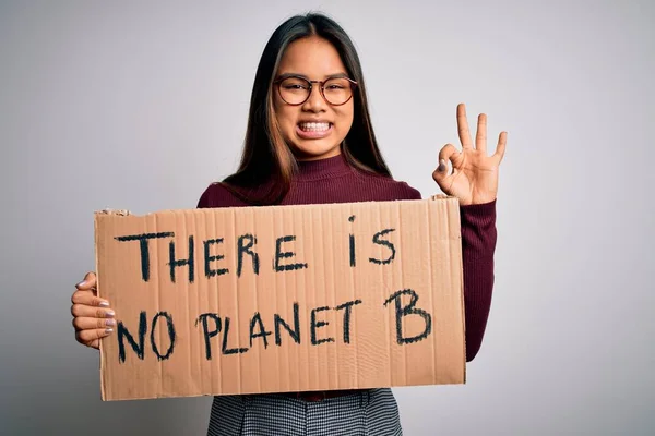 Young asian activist girl asking for environment holding banner with planet message doing ok sign with fingers, excellent symbol