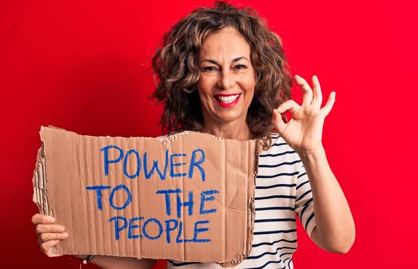 Senior woman asking for social movement holding banner with power to the people message doing ok sign with fingers, smiling friendly gesturing excellent symbol