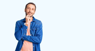 Gündelik giysiler giyen, kameraya kendinden emin, kolları çapraz ve çenesi havada gülümseyen genç yakışıklı bir adam. Olumlu düşünmek. 