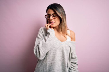 Genç, güzel esmer bir kadın pembe arka plan üzerine günlük süveter ve gözlük takıp diş ağrısı ya da diş ağrısı yüzünden acı dolu bir ifadeyle ağıza dokunuyor. Dişçi