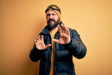 Sakallı, kar maskesi takmış, kar maskesi takmış, kel yakışıklı kayakçı. Tiksinti tepkisi yüzünden tiksinti ve tiksinti ifadesi takınıyor. Eller havada