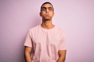 Yakışıklı Afro-Amerikan erkeği, rahat tişört ve gözlük takıp pembe arka plan şişiren komik suratlı. Havayla şişmiş ağız, çılgın bir ifade..