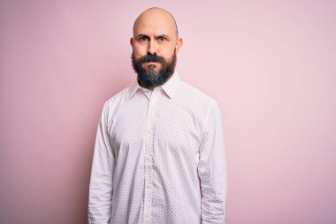 Yakışıklı, kel, sakallı, zarif tişörtlü, soyutlanmış pembe arka planda komik yüzlü yanakları olan bir adam. Havayla şişmiş ağız, çılgın bir ifade..