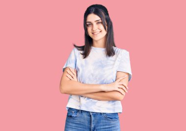 Gündelik tişört giyen, kolları çapraz gülümseyen ve kameraya bakan güzel bir kız. pozitif kişi. 