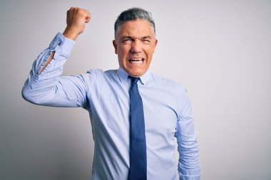 Orta yaşlı, yakışıklı, gri saçlı, şık gömlekli, kravatlı kızgın ve kızgın bir iş adamı öfkeyle bağırırken yumruğunu kaldırıyor. Öfke ve agresif kavram.