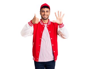 Beyzbol forması giyen genç İspanyol adam 6 numarayı gösterip işaret ederken kendinden emin ve mutlu gülümsüyor.. 