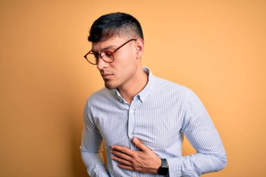 Sarı arka planda inek gözlüğü takan genç, yakışıklı İspanyol iş adamı. Midenin üstünde elleri olan. Çünkü hazımsızlık, acı verici bir hastalık. Ache kavramı.