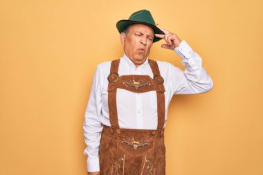 Sarı arka planda Alman geleneksel Ekim Festivali kıyafeti giyen yaşlı gri saçlı bir adam. Alnındaki sorun yüzünden endişeli ve stresli. Kriz konusunda endişeli.