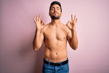 Sakalsız, sakalsız, genç ve güçlü bir adam pembe arka planda duruyor rahatlamış ve parmaklarıyla meditasyon hareketi yaparken gözleri kapalı gülümsüyor. Yoga konsepti.