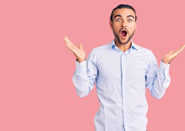 İş kıyafetleri giymiş genç yakışıklı adam çılgın ve başarıyı kollarını kaldırıp heyecanla haykırarak kutluyor. Kazanan konsept 