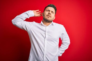 Mavi gözlü, zarif gömlekli genç bir iş adamı kırmızı izole edilmiş arka planda duruyor yorgun ve rahat, uykulu ve sabahın erken saatlerinde esniyor.