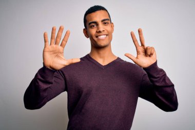 Beyaz arka plan üzerine gündelik süveter giyen genç ve yakışıklı Afro-Amerikan adam sekiz numaralı parmaklarıyla işaret ederken kendinden emin ve mutlu gülümsüyor..