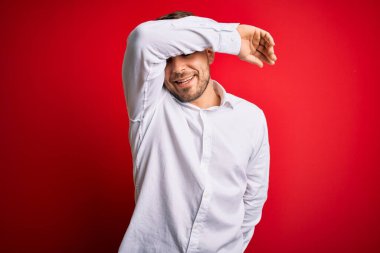 Mavi gözlü, zarif gömlekli genç bir iş adamı. Kırmızı izole edilmiş arka plan üzerinde duruyor. Gözleri, neşeli ve komik bir şekilde gülümsüyor. Kör kavram.