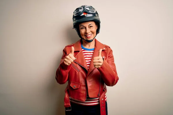 白地成功サインの上にオートバイのヘルメットとジャケットを身に着けている中世のオートバイの女性は手で肯定的なジェスチャーを行う 親指を笑顔と幸せ 陽気な表情と勝者のジェスチャー — ストック写真