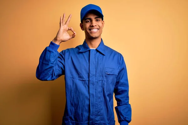 年轻的非洲裔美国技师 身穿蓝色制服 头戴黄色背景帽 微笑着 手指手画脚地签了名 成功表达 — 图库照片
