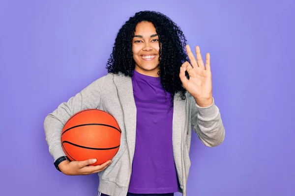 アフリカ系アメリカ人の女性が指でOkサインを行う紫色の背景にバスケットボールボールを保持スポーツをやって 優れたシンボル — ストック写真