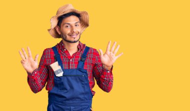 Yakışıklı Latin Amerikalı, giyimli, tamirci üniforması giyen dokuz numaralı parmaklarıyla kendini beğenmiş ve mutlu gülümseyen genç adam.. 