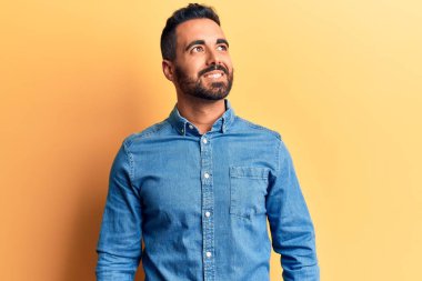 Gündelik kıyafetler giyen genç İspanyol bir adam yüzünde gülümsemeyle yan yana bakıyor, doğal bir ifade. Kendinden emin gülen. 