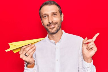 Elinde kağıt uçak tutan genç yakışıklı adam gülümsüyor. 