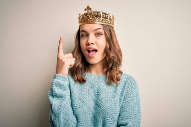 Soyutlanmış arka planda kraliçe tacını takan genç sarışın kız başarılı bir fikri işaret ediyor. Heyecanlı ve mutlu. Bir numara..