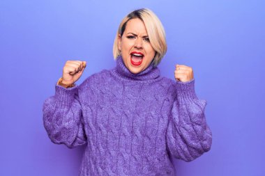Güzel sarışın ve cüsseli bir kadın mor arka plan üzerine balıkçı yaka kazak giyiyor kızgın ve kızgın yumruklar sallarken öfkeyle bağırıyor. Öfke ve agresif kavram.