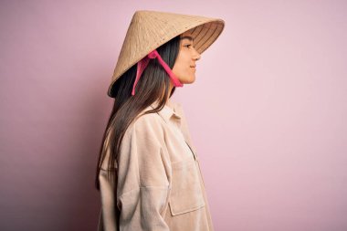 Geleneksel konik Asya şapkası takan genç ve güzel bir kadın pembe arka planda, yan tarafa bakıyor, rahat profil pozu veriyor, kendine güvenen bir gülümsemesi var..