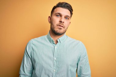 Sarı arka planda zarif yeşil gömlek giyen mavi gözlü genç iş adamı yüzünde ciddi bir ifadeyle rahatladı. Basit ve doğal bir şekilde kameraya bakıyorsun..