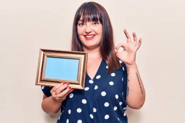 Elinde boş bir çerçeve olan genç bir kadın parmaklarıyla imza atıyor, gülümseyerek mükemmel bir sembol oluşturuyor. 