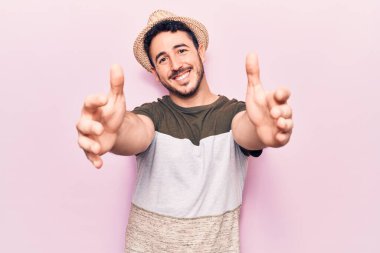 Gündelik giysiler giymiş genç İspanyol adam kameraya bakıp sarılmak için kollarını açmış gülümsüyor. Mutluluğu kucaklayan neşeli bir ifade.. 