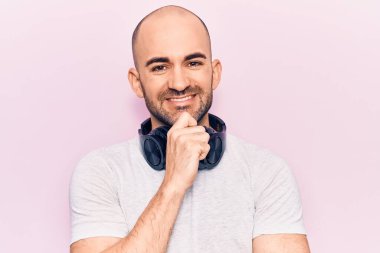 Genç yakışıklı kel adam müzik dinliyor kulaklık takıyor gülümsüyor ve kameraya kollarını kavuşturup çenesine bakıyor. Olumlu düşünmek. 