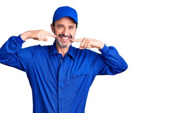 Orta yaşlı yakışıklı tamirci üniforması giyen neşeli bir şekilde gülümseyen ve parmaklarıyla ve ağzıyla işaret eden bir adam. diş sağlığı kavramı. 