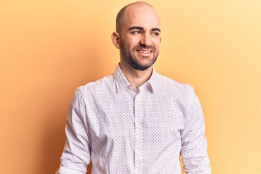 Zarif bir gömlek giyen genç yakışıklı kel bir adam, yan bakmak için, rahat profil pozu doğal bir yüz ve kendinden emin bir gülümseme ile. 