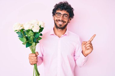 Kıvırcık saçlı yakışıklı genç adam ve elinde bir buket beyaz çiçekle mutlu bir şekilde gülümsüyor. 