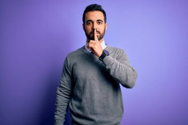 Sakallı, sıradan bir kravat takan, mor arka planda duran yakışıklı bir iş adamı sessiz olmak istiyor. Sessizlik ve gizli konsept.