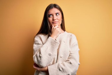 Mavi gözlü genç bir kadın sarı arka planda dikilmiş soru soran, düşünceli bir ifade takınıyor. Düşünceli bir yüzle gülümsüyor. Şüphe kavramı.